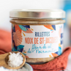 Jar of scallops rillettes on a towel with some fleur de sel in a wooden spoon in the foreground
