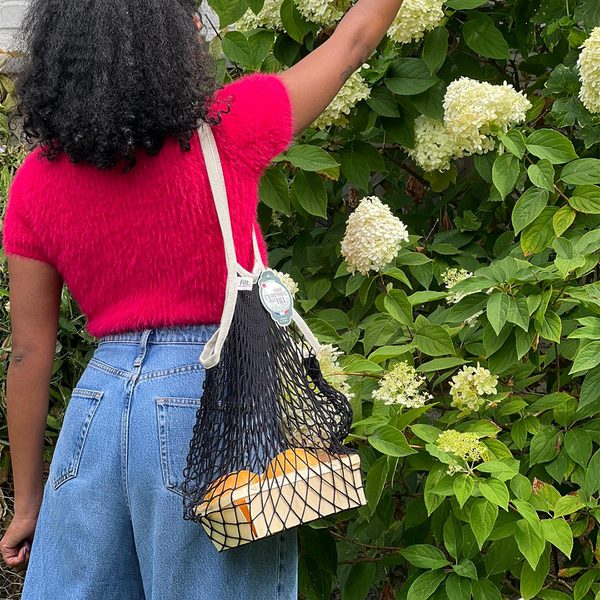 Black écru Filt 1860's 100% cotton net shopping bag on someone's shoulder with fruits in it