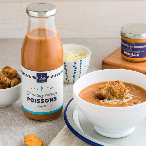 Bottle of La Perle des Dieux' fish soup, with some served in a bowl and a jar of rouille in the background.