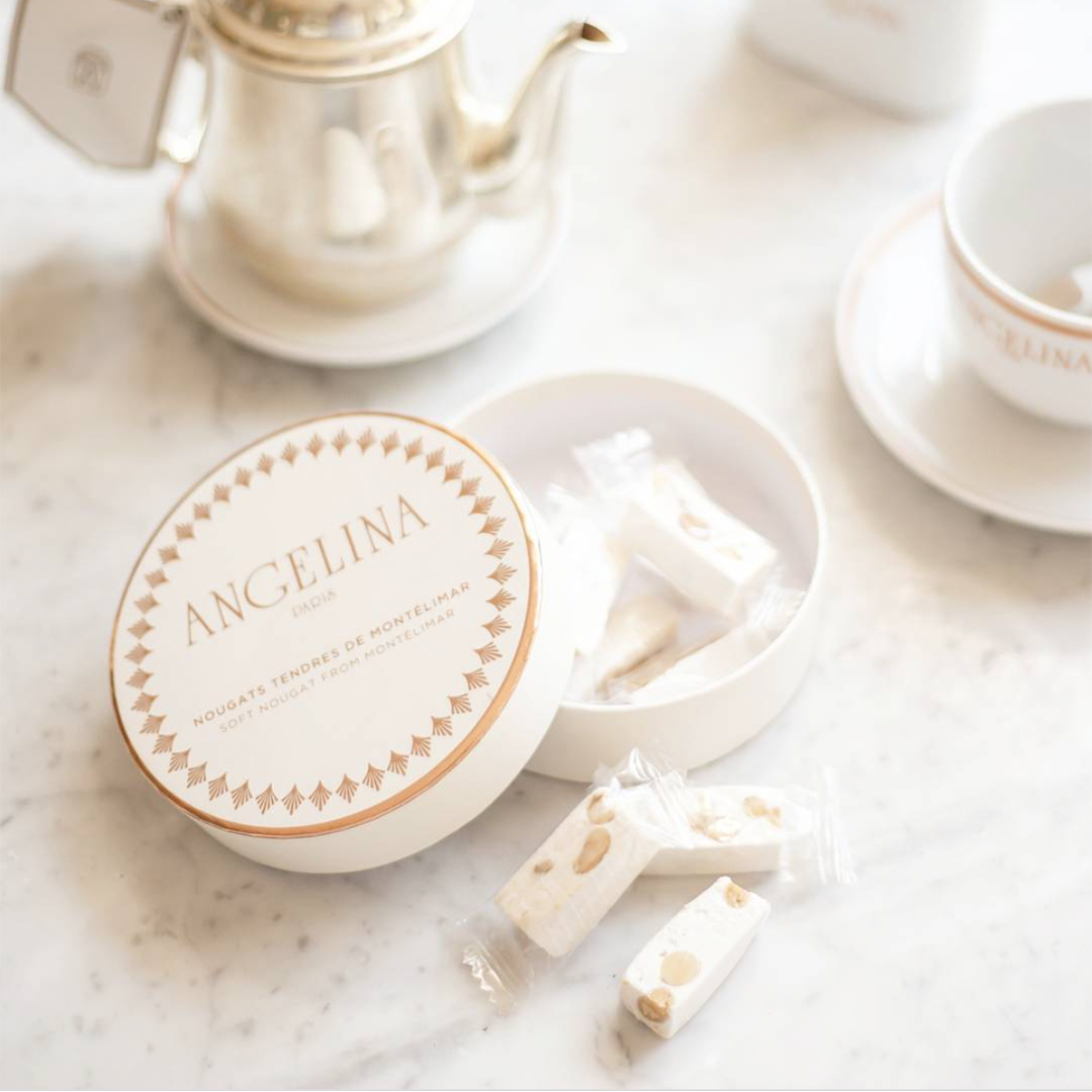 Soft nougat from Montélimar in Angelina's prestigious round shaped box, half opened & displayed on table with teapot and teacup.