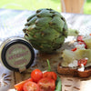 in the forehead, two toasts with artichokes, tomatoes, cheese and salad and at the back, a jar of Maison Bremond 1830's Artichoke & Basil Pulp with a artichoke on the side. 