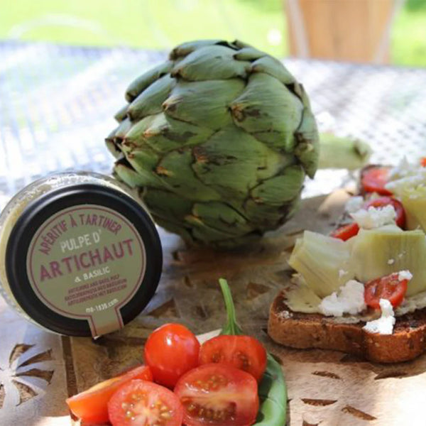 in the forehead, two toasts with artichokes, tomatoes, cheese and salad and at the back, a jar of Maison Bremond 1830's Artichoke & Basil Pulp with a artichoke on the side. 