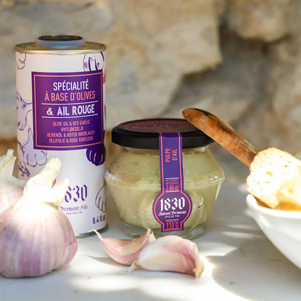 Jar of Maison Bremond 1830's garlic cream with fresh garlic in the foreground and a bottle of oil in the background.