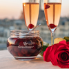 Opened jar of Distilleries Peureux' griottines displayed with 2 flutes of champagne and a rose.