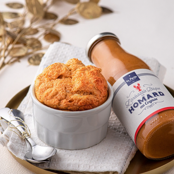 Bottle of lobster bisque with cognac on a plate with a soufflé  pastry made this lobster bisque, and a spoon