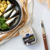 La Perle des Dieux' tin of sardines with churned butter to grill. Some sardines in a pan with potatoes in the background.